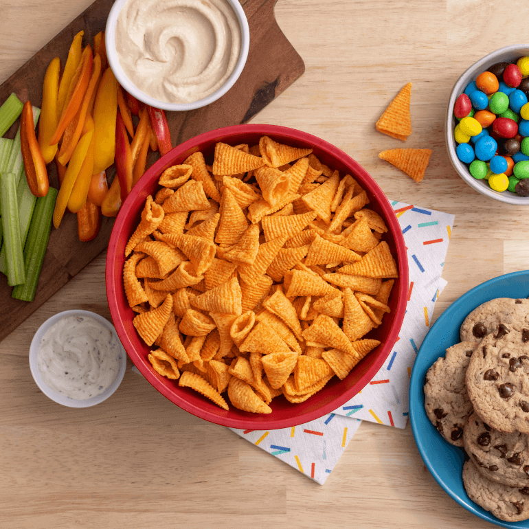 Bowl of Nacho Bugles, chopped veggies, cookies and candy on a wooden table